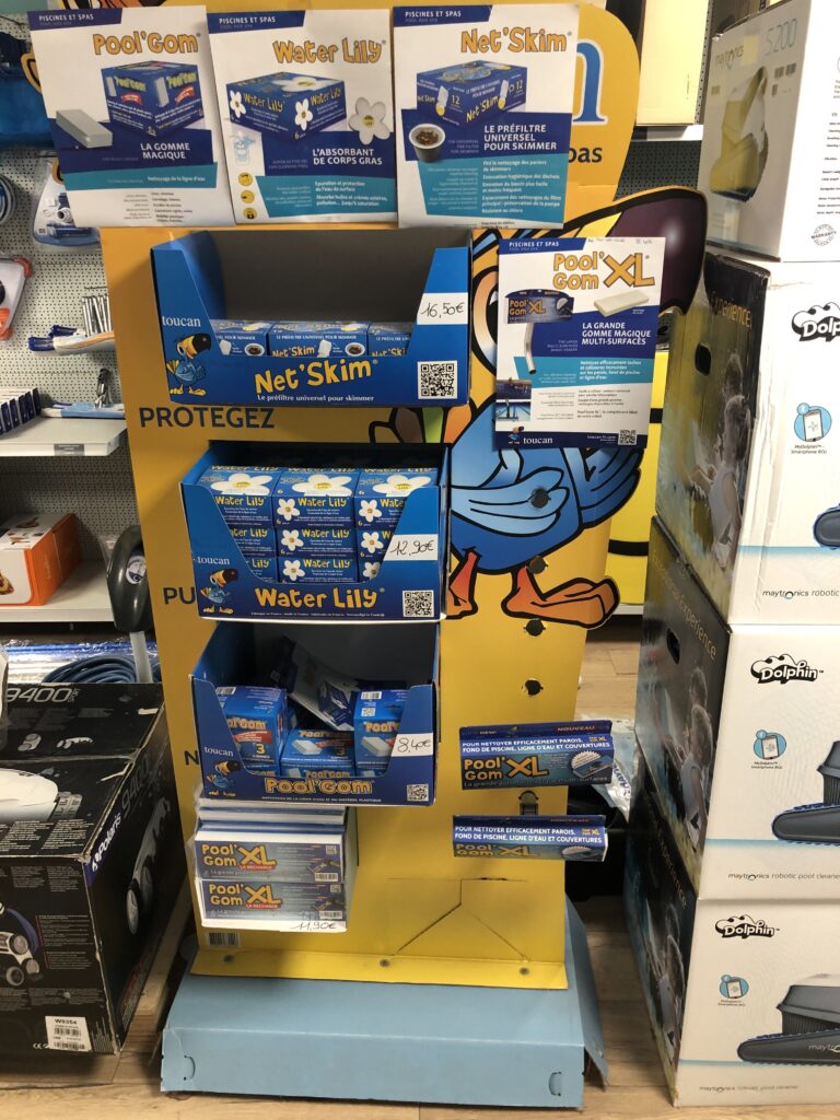 Présentoir Toucan jaune produits piscine: Pool'Gom (gomme magique), Water Lily (absorbant), Net'Skim (préfiltre skimmer). Prix 8,40€-16,50€.