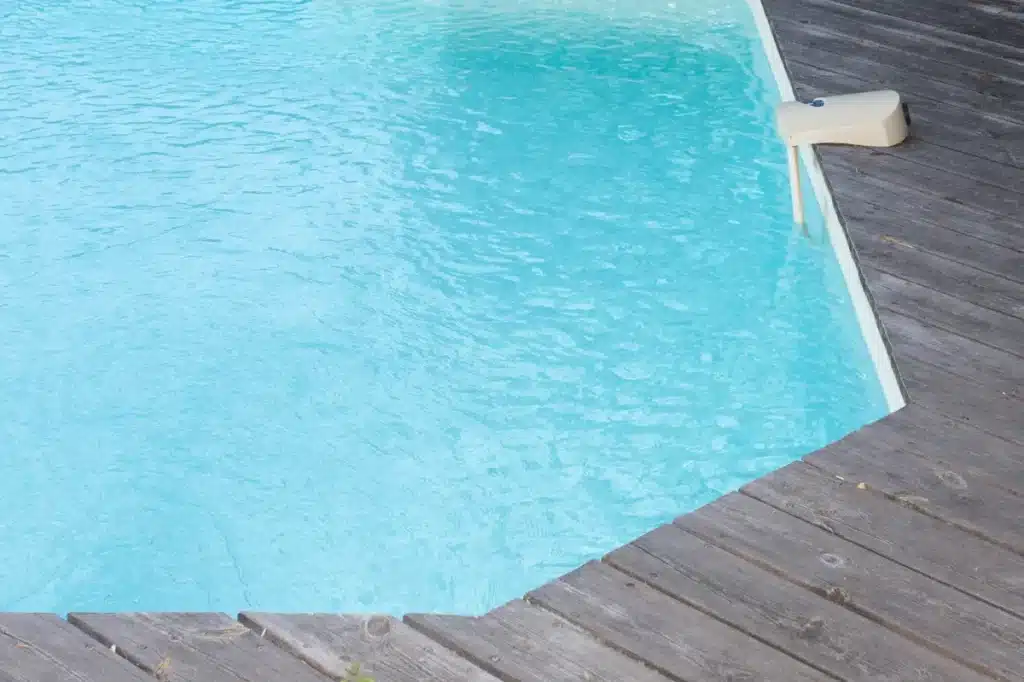 Piscine à l'eau bleue claire avec ondulations, bordée par une terrasse en bois patiné et un appareil beige flottant.